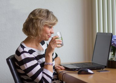 Attractive middle-aged woman looking at the monitor and drinking clipart