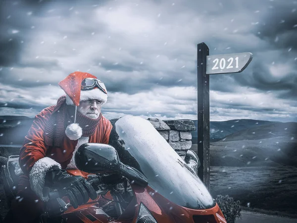 Ciddi Noel Baba 2021 yılına kırmızı bir motosikletle daldı. Atlı ve kar fırtınalı serin bir kış manzarasına karşı..