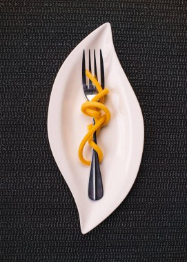 Beyaz tabakta bir çatalla makarnayı kapat, küçük porsiyon, desenli siyah arkaplan, yukarıdan görünüm.