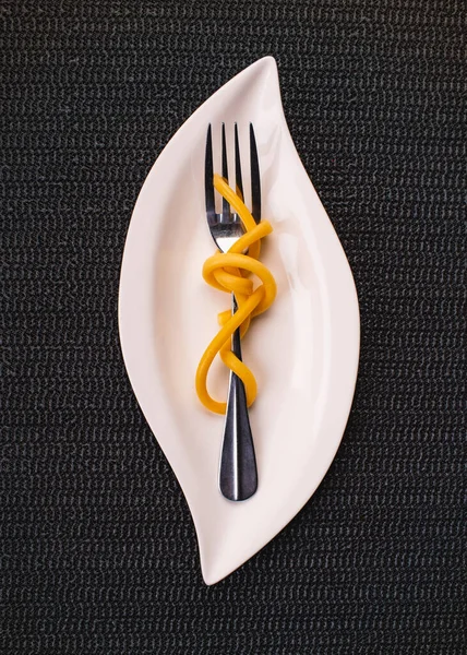 Beyaz tabakta bir çatalla makarnayı kapat, küçük porsiyon, desenli siyah arkaplan, yukarıdan görünüm.