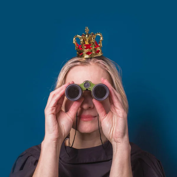 A woman with a crown on her head looks through binoculars. The concept of planning a vacation or future in life.