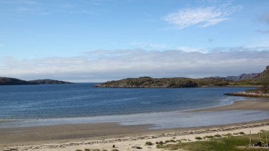 Barents Denizi sahili manzarası. Barents Denizi koyunun koyu mavi suyu. Denizde küçük taş adalar. Dalgalar çekildiğinde deniz. Güneşli bir günde deniz manzarası. Mavi gökyüzünün altında güzel bir kıyı şeridi.