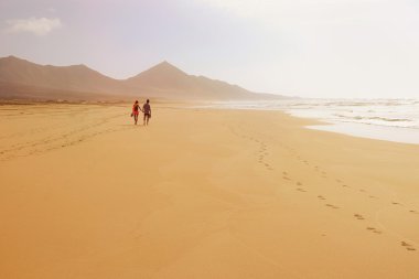 A couple walking holding hands on the beach Cofete on Fuertevent clipart