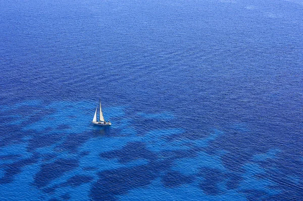 A boat with a white sail in a blue sea