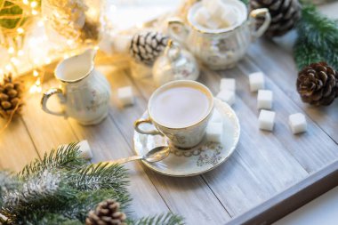 Rafine şekerli, eski bir porselen servisinden alınmış sütlü bir fincan İngiliz çayı. Çelenklerin ve köknar dallarının arka planında Noel çayı partisi kahvaltısı..