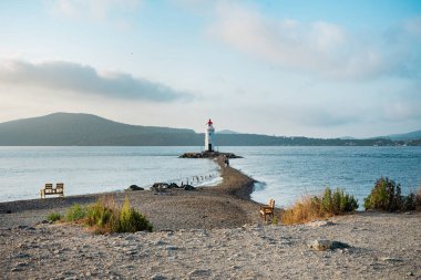 Deniz kıyısında kırmızı çatılı eski bir deniz feneri. Deniz Burnu. Seyahatten kartpostal.