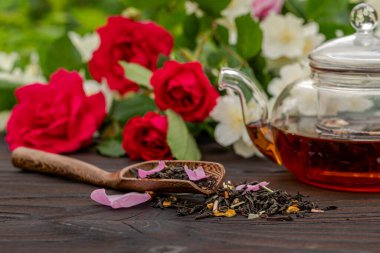 Güllerin ve yasemin çalılarının arasında çay eşliğinde bambu kaşığının kesilmiş görüntüsü. Açık hava, piknik, kahvaltı. Bulanık cam çaydanlık.