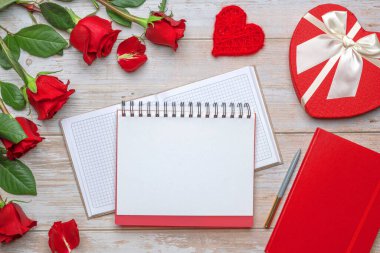 Açık ekose defter, kalp şeklinde hediye kutusu saten fiyonk, güller ve yapraklar, ip şeklinde sevgililer günü kartı, ahşap yüzey. 14 Şubat, nişan, evlilik yıldönümü, romantik akşam planları..