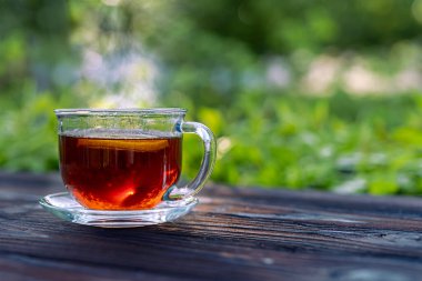 Ahşap bir masada çay ve limonlu dumanı tüten cam bardak. Kısa DOF ile seçici odaklanma. Görüntüyü kapat.