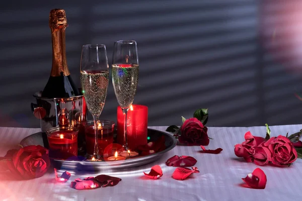 アイスバケツに入ったボトル スパークリングワインのグラス キャンドル付きのトレイ 赤いバラと花びらの装飾 白いリネン シルエットや影とブランチ壁 新婚旅行かバレンタインデーかロマンチックな夜愛の夜か — ストック写真