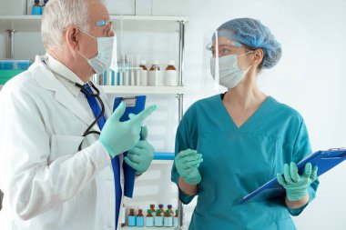 Beyaz önlüklü kıdemli doktor ve kadın sağlık görevlisi belgeleri mavi klasörde inceleyip hastanede tartışıyorlar.