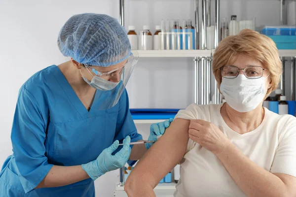 Yetişkin yaşlı bayana aşıyı enjekte eden profesyonel bir kadın. Açık hava hastanesi sağlık durumu
