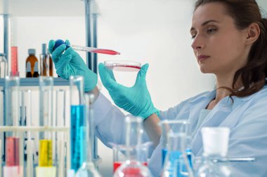  Cropped view of smart active woman laboratory assistant holding petri dish, pipetting liquid