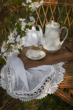 Güneşli bir günde beyaz bir masa örtüsünde kahve seti, kiraz çiçeği, kek, puding, çikolata, kakao. Açık hava, piknik, brunch, bahar havası. Yumuşak odak