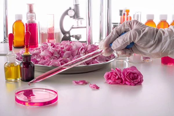 A gloved hand holds a dropper over a Petri dish in a modern perfume laboratory. The background is blurred.