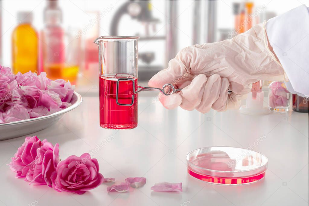 A hand in a glove holding a clip with a test tube in up-to-date perfume laboratory. Background blurred