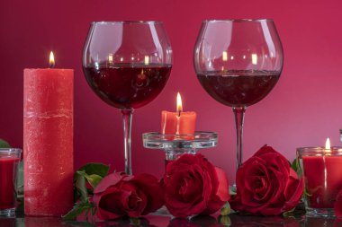 Şeffaf şamdanlardaki kırmızı mumlar kırmızı arka plandaki ayna yüzeyinde güllerle çevrili bardakları şarapla aydınlatıyor. Sevgililer Günü ya da romantik akşam daveti