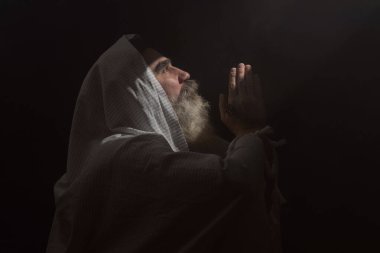 A senior man standing in dark smoky background light ray from above. Prayer gesture. clipart