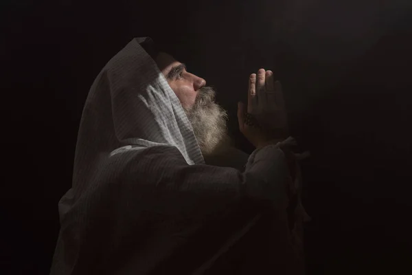 Yukarıdan gelen koyu dumanlı arka plan ışık huzmesinin içinde son sınıf öğrencisi. Dua jesti.