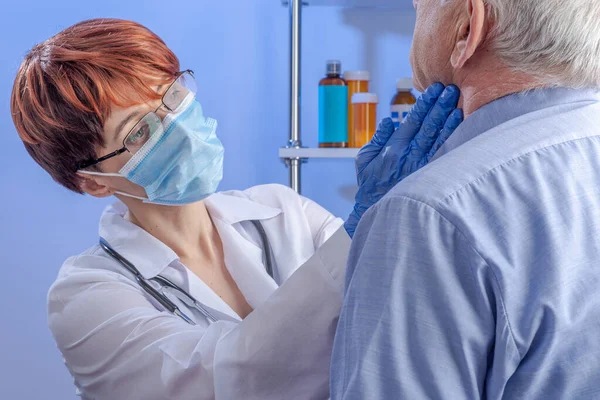 Compassionate female doctor in white coat and mask put her gloved hands on the neck of senior male patient. Professional medical care in the hospital.