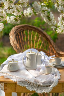 Elegant coffee set, lace tablecloth, cherry blossom branches, wooden table. Outdoor breakfast, picnic, brunch, spring mood. Soft focus