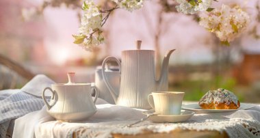 Coffee set on a white tablecloth on a sunny day, cherry blossom, cupcake. Outdoor, picnic, brunch, spring mood. Soft focus