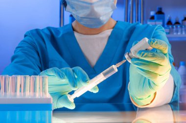 Hastanede sağlık görevlisinin elinde şırınga ve ampul uyuşturucu vardı. Yansımalı cam masa üstü. Mavi ultraviyole ışıklandırma kuartzizasyonu steril odası. Görüntüyü kapat