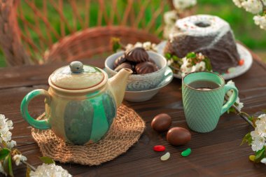 Paskalya brunch 'ı. Çay takımı, çikolatalı puding, kek ve renkli yumurtalar, fasulye şekilli lolipoplar, çiçek açan kiraz dalları, ahşap masa örtüsü.