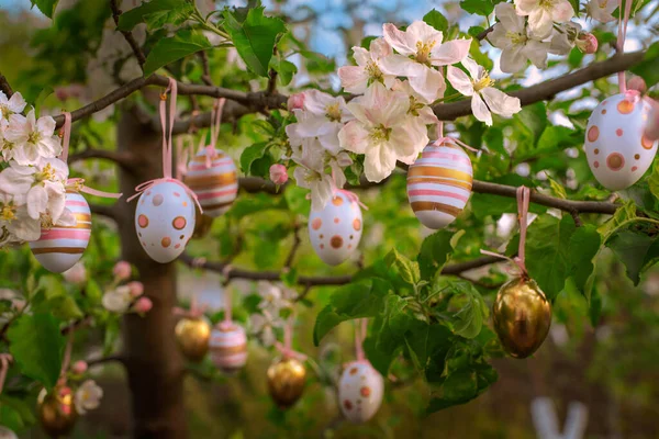 Bahçedeki ya da parktaki ağaçta çiçek açan elma dalları üzerinde süsleme yumurtaları. Çizgili ve benekli pembe ve altın süsler..