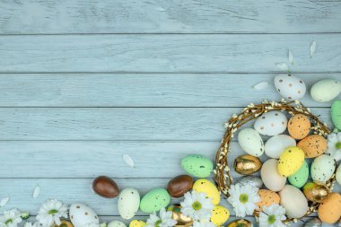 Paskalya tebrik kartı, takvim, poster, afiş. Çikolata, altın, dekoratif yumurta, papatya çiçeği, açık mavi tahta üzerinde çelenk.