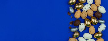 Paskalya tebrik kartı, takvim, poster ve afiş için modern tebrik arkaplanı. Çikolata, altın, dekoratif yumurtalar, derin mavi bir yüzeyde