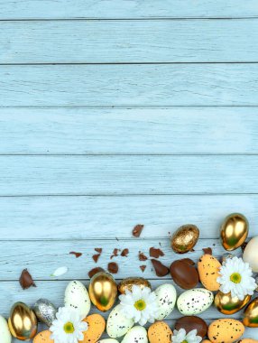 Paskalya tebrik kartı, takvim, poster, afiş. Çikolata, altın, dekoratif yumurta, papatya çiçeği, açık mavi tahta üzerinde