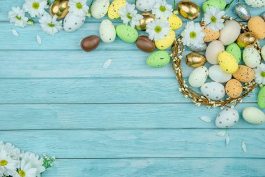 Paskalya tebrik kartı, takvim, poster, afiş. Çikolata, altın, dekoratif yumurta, papatya çiçeği, açık mavi tahta üzerinde çelenk.