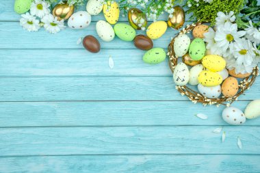Paskalya tebrik kartı, takvim, poster, afiş. Çikolata, altın, dekoratif yumurta, papatya çiçeği, açık mavi tahta üzerinde çelenk.
