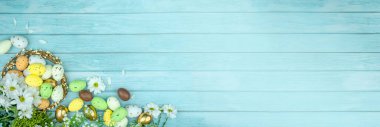 Paskalya tebrik kartı, takvim, poster, afiş. Çikolata, altın, dekoratif yumurta, papatya çiçeği, açık mavi tahta üzerinde çelenk.