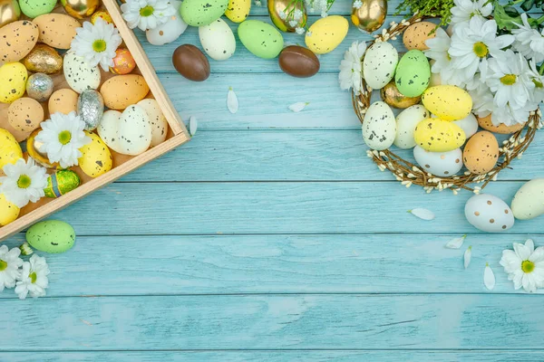 Paskalya tebrik kartı, takvim, poster, afiş. Çikolata, altın, dekoratif yumurta, papatya çiçeği, açık mavi tahta üzerinde çelenk.