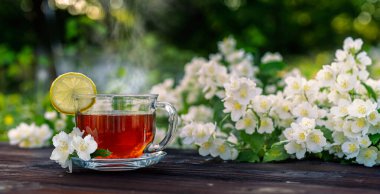 Bardakta çay, limon, ahşap bir masada yasemin dalları. Açık hava, piknik, kahvaltı.