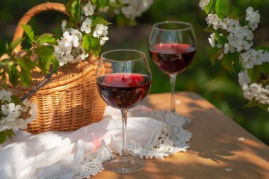 Baharda bahçede şarap tatma partisi. Güzel bir ilkbahar gününde, tahta bir masada, uzun, saplı bardaklarla, kırmızı şarapla dolu bir hayat. Kiraz çiçekleriyle çiçek açan dallar. Seçili odak
