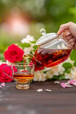 Çiçek açan gül ve yasemin çalılarının arasından zarif fincanlara el yapımı çay dökülüyordu. Açık hava, piknik, kahvaltı. Yeşil yapraklar bulanık. Jete odaklan.