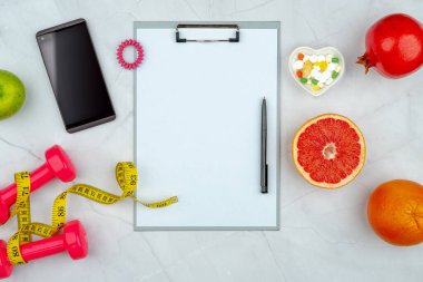 Eğitim ekipmanları, kalp şeklindeki plaka, diyet takviyesi hapları, akıllı telefon, dambıl ve mezura ile sağlıklı yaşam tarzı idmanı konsepti. Boş kopyalama alanı, kırpma tahtası maketi.