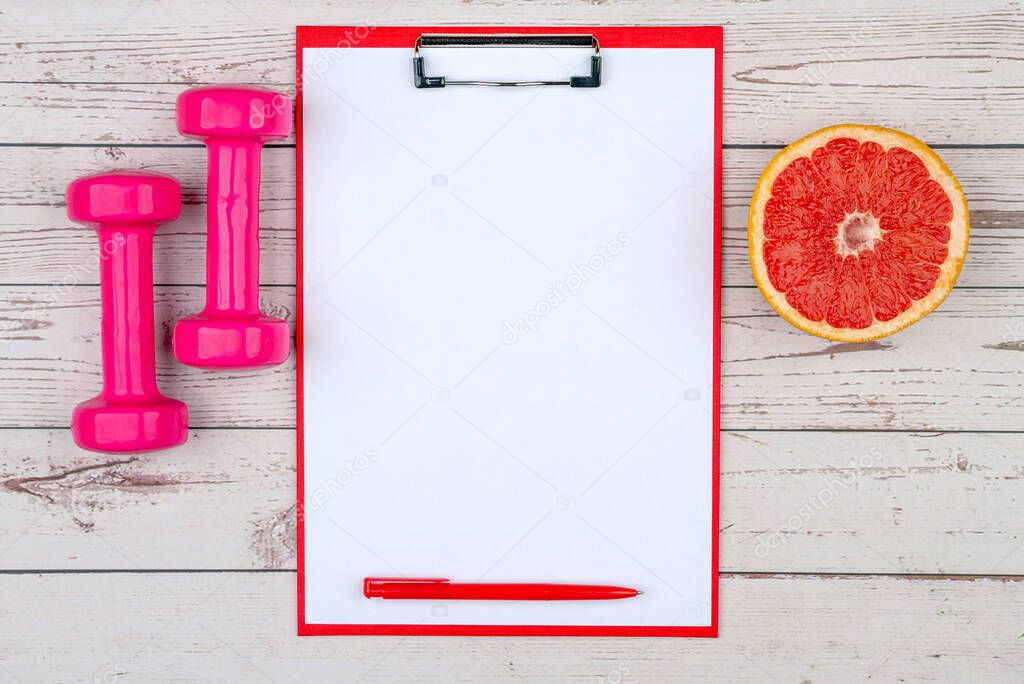 Healthy lifestyle workout concept with training equipment. The idea of how to achieve harmony and longevity while doing sports. Empty copy space, dumbbells, clip board, grapefruit.