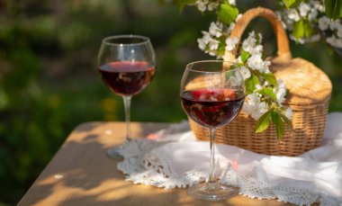 Baharda bahçede şarap tatma partisi. Güzel bir ilkbahar gününde, tahta bir masada, uzun, saplı bardaklarla, kırmızı şarapla dolu bir hayat. Kiraz çiçekleriyle çiçek açan dallar. Seçili odak, kopyalama bölmesi