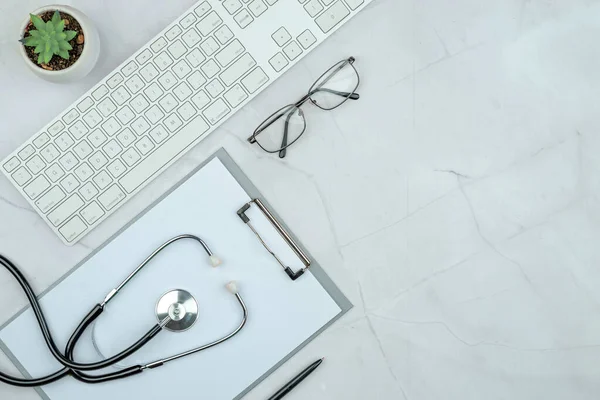 Modern marble work table at the doctor\'s appointment. Keyboard, stethoscope, glasses. Purity, white and grey color, flat lay. Empty copy space, clip board mock up