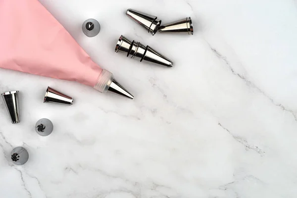 Pasta poşeti krem pembesi enjektörü pasta tatlı dekorasyonu için, malzeme seti krema boruları, paslanmaz çelik başlık uçları. Beyaz mermer arka planda DIY araçları. Fotokopi alanı ile fırın kavramı