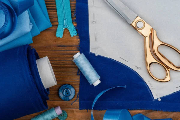 Özel dikim giysiler, dikiş aksesuarları. Makas, iplik, dikiş deseni, ahşap bir masada mavi kumaşlar..