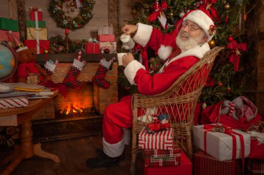 Noel Baba şöminenin ve Noel ağacının yanında. Ahşap evin içindeki şenlikli iç mekan, Noel 'in neşeli ruhu. Gerçek beyaz sakallı son sınıf öğrencisi Noel Baba kostümü giyiyor..