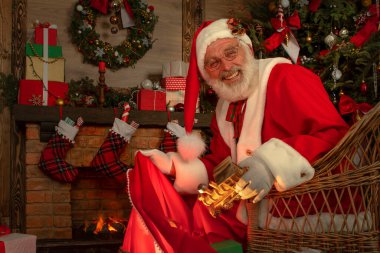 Noel Baba hediye dolu bir çantayla şömine ve Noel ağacının yanında. Ahşap evin içindeki şenlikli iç mekan, Noel 'in neşeli ruhu. Gerçek beyaz sakallı son sınıf öğrencisi Noel Baba kostümü giyiyor..