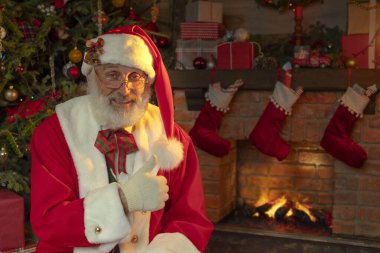 Noel Baba şöminenin ve Noel ağacının yanında. Ahşap evin içindeki şenlikli iç mekan, Noel 'in neşeli ruhu. Gerçek beyaz sakallı son sınıf öğrencisi Noel Baba kostümü giyiyor..