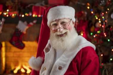 Noel Baba şöminenin ve Noel ağacının yanında. Ahşap evin içindeki şenlikli iç mekan, Noel 'in neşeli ruhu. Gerçek beyaz sakallı son sınıf öğrencisi Noel Baba kostümü giyiyor..