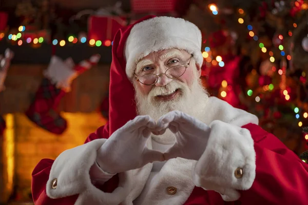 Noel Baba, elleri şöminenin ve Noel ağacının yanında kalp şekli veriyor. Ahşap evin içindeki şenlikli iç mekan, Noel 'in neşeli ruhu. Gerçek beyaz sakallı son sınıf öğrencisi Noel Baba kostümü giyiyor..